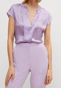 Lavendel satinblus med djup V-ringning, kort ärm och subtila veckdetaljer, kombinerad med matchande lavendel skräddarsydda byxor.