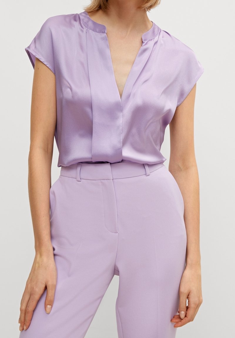 Lavendel satinblus med djup V-ringning, kort ärm och subtila veckdetaljer, kombinerad med matchande lavendel skräddarsydda byxor.