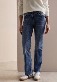 Jeans de denim azul claro con corte recto, bolsillos frontales y un ligero desvanecimiento. Combinados con zapatillas blancas con detalles en negro.