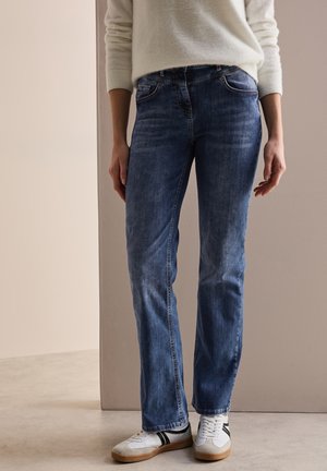 Jean en denim bleu clair avec une coupe droite, des poches avant et un léger effet dégradé. Assortis à des baskets blanches avec des accents noirs.