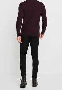 Maglione borgogna con collo a giro, maniche aderenti e orlo a costine, abbinato a pantaloni neri su misura e stivali alla caviglia. Tessuto a maglia liscia.