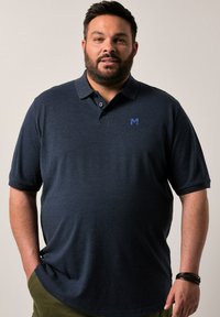 Námořnická modrá polo tričko s krátkým rukávem, se subtilní texturou, dvěma knoflíky na límci a malým modrým logem "M" na hrudi.