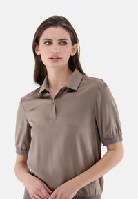 Kurzärmliges Polohemd aus weichem beigen Stoff. Verfügt über einen Kragen und eine Knopfleiste sowie elastische Bündchen. Glatte Oberfläche mit einem dezenten Glanz.