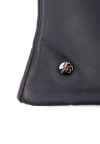 Eck einer schwarzen Lederhandtasche mit glatter Textur, dreieckiger Form und einem glänzenden silbernen Akzentknopf mit geprägt Logo.