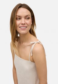 Top de lino en beige claro, con tirantes delgados y lazos ajustables, y un diseño de corte recto. Textura suave y estilo minimalista.