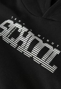 Sudadera negra con un llamativo texto en blanco a rayas que dice "TÓMATE UN MINUTO Y VUELVE A LA ESCUELA", con un fondo de tejido texturizado.
