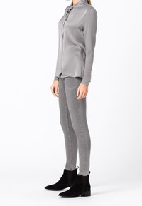Blusa grigia in satin a maniche lunghe, abbinata a jeans fitted grigi chiari. Stivali ankle in suede neri con punta appuntita e tacco a blocco.