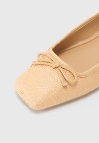 Ballerine tissée beige avec un bout carré. Elle présente un accent en nœud fait du même matériau sur le dessus et une doublure intérieure lisse.