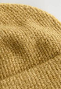 Soft, ribbed knit fabric in mustard yellow with fuzzy texture and visible stitching, likely part of a warm garment or accessory.
