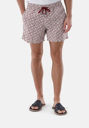 Rote und weiße bedruckte Badeshorts mit elastischem Bund und verstellbarem Kordelzug, kombiniert mit schwarzen Slidesandalen mit Kreuzriemen.