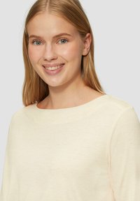 Lichtbeige lange mouwen top met een ronde hals. De stof lijkt zacht met een subtiele structuur en een lichte glans.