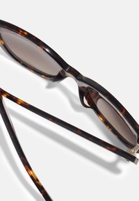 Tortoiseshell sunglasses with a rounded frame, dark gradient lenses, and slender arms featuring metallic accents near the hinges.