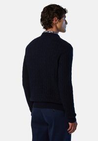 Maglione blu navy a maglia con motivo a cavo in rilievo, polsini e orlo a costine, design a collo rotondo, indossato sopra una camicia a quadri, vista da dietro.