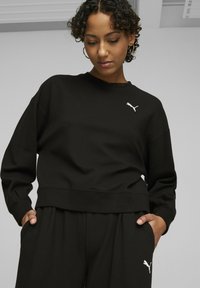 Czarny, strukturalny sweatshirt z żebrowanym dołem i mankietami, z białym logo Puma na piersi. Połączony z dopasowanymi czarnymi spodniami.