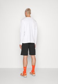 Hvit langermet skjorte, svarte cargo-shorts, oransje sokker og sneakers. Klart, minimalistisk design med funksjonelle lommer og kontrasterende farger.