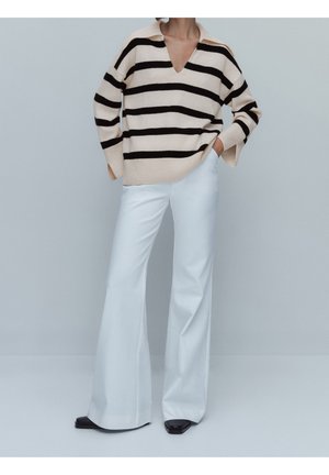Pull en maille rayé beige et noir avec un col en V profond et des manches larges, associé à un pantalon évasé blanc taille haute et des chaussures à talons carrés noires.