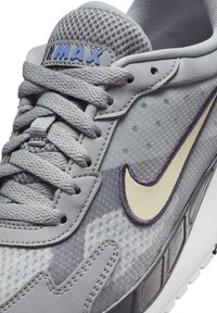 Nike Air Max cipők szürke halszövetből és szintetikus anyagból, lila Nike logóval, szürke fűzővel és strukturált részletekkel.