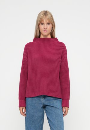 Sweater malha magenta com colarinho alto e largo e textura canelada; apresenta ombros caídos e mangas longas. Usado com jeans azuis.