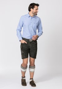 Camicia a scacchi blu con bottoni, pantaloni corti in pelle grigia, caratterizzati da ricami decorativi, bottoni in metallo, abbinati a calze a motivi fino al ginocchio.