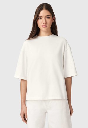 Hvid, oversize t-shirt lavet af glat stof. Korte ærmer, rund halsudskæring og en afslappet pasform. Kombineret med hvide bukser.