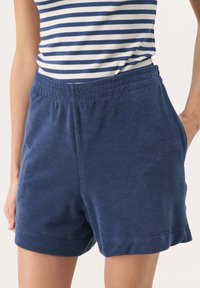 Pantaloni corti in pile blu navy con vita elasticizzata, dotati di tasche laterali e una texture morbida, che terminano appena sopra il ginocchio.