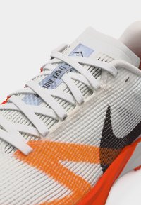 Λευκό αθλητικό παπούτσι με υφασμάτινη υφή, πορτοκαλί λεπτομέρειες, μαύρο λογότυπο Nike και λευκά κορδόνια δεμένα πάνω σε ετικέτα που γράφει "TERRA KIGER".