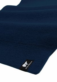 Sciarpa lavorata a maglia blu navy con un motivo testurizzato e un'etichetta nera con logo bianco su un lato. Il tessuto appare morbido e flessibile.