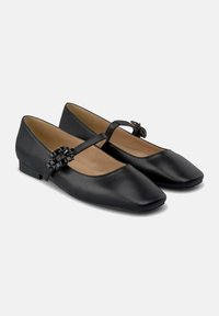 Zapatos planos de cuero negro con punta cuadrada y tacón bajo. Presentan una correa decorativa y un acento texturizado en la parte frontal. Acabado mate suave.