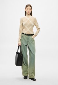 Pulover cu guler înalt, bej cu model, cu mâneci lungi, asortat cu blugi largi, de culoare verde deschis, și o geantă tote neagră. Botine negre completează ținuta.