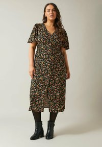 Abito midi floreale con maniche corte a volant, sfondo nero, fiori multicolori, scollo a V e orlo arricciato; abbinato a stivaletti neri alla caviglia.