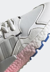 Białe sneakersy z teksturowanymi materiałami, szarymi akcentami oraz charakterystyczną wyściełaną podeszwą z gradientem od białego do różowego i niebieskimi wykończeniami.