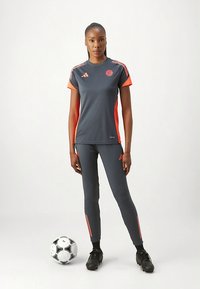 Halli spordipluus oranžide detailide ja logoga, sobitatud samast hallist retuusidega. Mustad jalgpallikingad ja pall täiendavad sportlikku välimust.