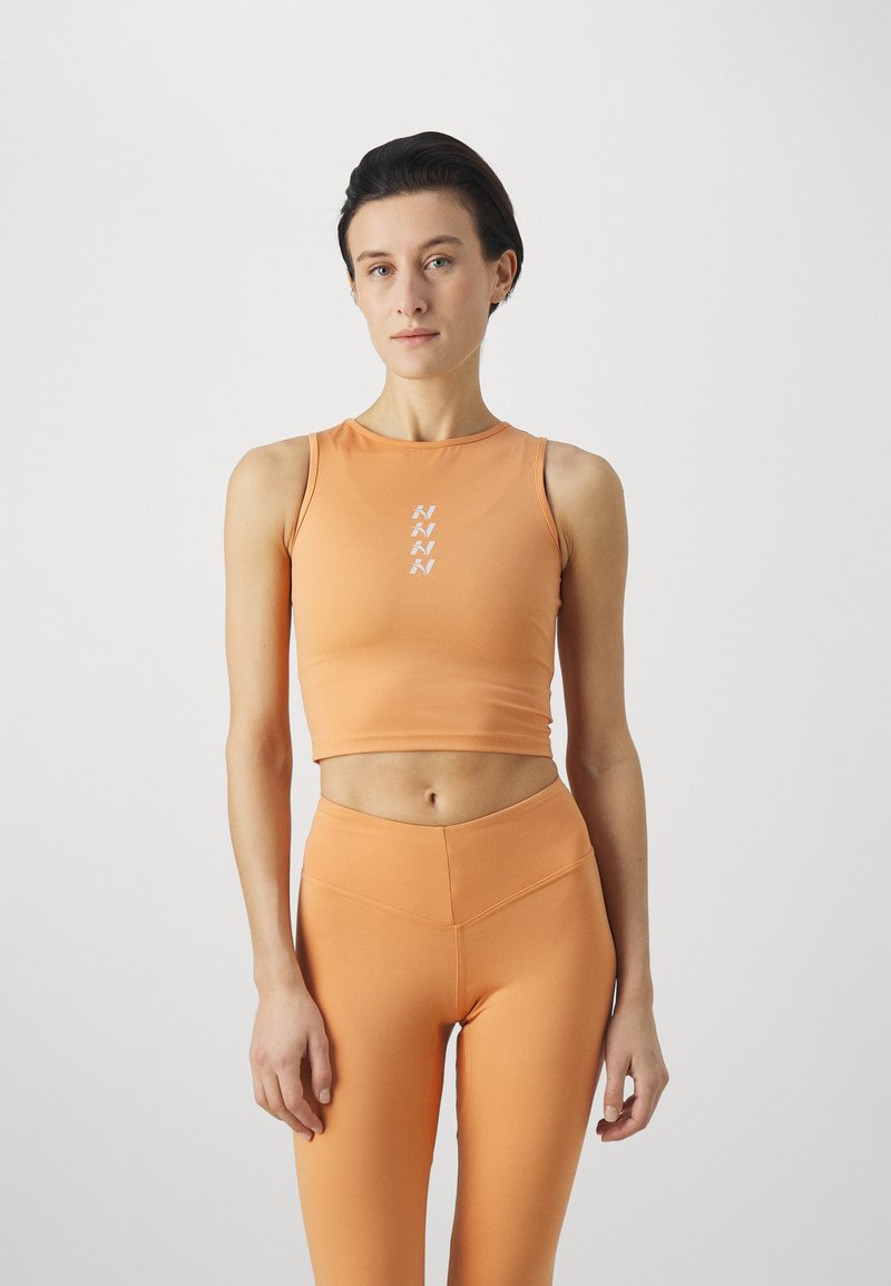 Oranžový sportovní top s krátkým rukávem a kulatým výstřihem, doplněný vysokými legínami. Top zdobí vertikální bílý detail s logem. Hladká textura.