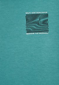 Turkos crewneck t-shirt i mjuk bomull, med en texturerad svart grafisk design och vit text som lyder "SALT DOG WORLDWIDE" och "REFINE THE ORDINARY."