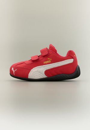 Κόκκινο αθλητικό παπούτσι Puma με λευκή λωρίδα με λογότυπο, μαύρη σόλα και δύο λουράκια με βέλκρο σε ουδέτερο φόντο.