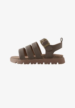 Brown leather sandal with four straps, adjustable brass buckle, thick textured sole, and heel loop for easy wear.
