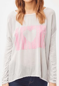 Camiseta de manga larga gris claro con un gráfico de corazón a rayas rosas. Mangas texturizadas y un ajuste holgado, con un escote redondo.