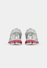 Baskets de sport grises avec accents métalliques, talon translucide et amorti rouge. Présentent une tige en mesh texturé et un motif géométrique unique sur le talon.