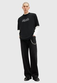 Sort oversized t-shirt med grafisk print lagd over en hvid langærmet skjorte, kombineret med sorte brede jeans og chunky sorte sko.