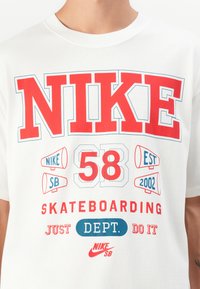 White t-shirt featuring bold red and blue screen-printed text. Design includes "NIKE," "SB," "58," and "SKATEBOARDING" with graphic accents.