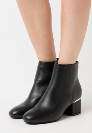 Bottes de cheville en cuir noir avec une texture lisse, bout rond et un talon épais orné d'un détail argenté.