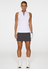 Vit ärmlös golftröja med hög krage och svarta detaljer, kombinerad med en grå kjol. Inkluderar en vit handske och sportskor.