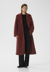 Cappotto in lana bordeaux con design doppiopetto, rever a punta e grandi bottoni neri. Taglio lungo e dritto con tessuto texture.