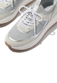 Grijze sneakers met een mesh body, suède accenten en witte veters. Heeft een gestructureerd patroon en een rubberen zool met een lichtbruine onderkant.