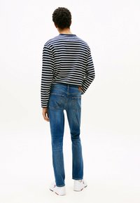 Camisa de manga larga a rayas con rayas azul marino y blancas, combinada con unos vaqueros de mezclilla azules que presentan un parche de cuero y dos bolsillos traseros.