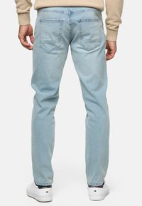 Jeans de mezclilla azul claro con un corte recto, que presentan dos bolsillos traseros y costuras en tono. Combinados con zapatillas deportivas blancas.