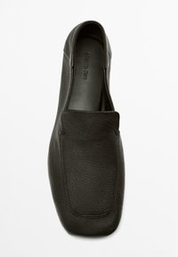 Chaussure noire en cuir à enfiler avec une texture lisse, un bout arrondi et un design minimaliste. Présente des coutures discrètes et une semelle plate.