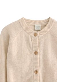 Beżowy sweter z dzianiny z okrągłym dekoltem, rękawami raglanowymi oraz brązowymi, drewnianymi guzikami z przodu. Miękka, fakturowana tkanina.