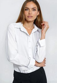 Biała koszula na guziki z kołnierzykiem i długimi rękawami, o gładkiej fakturze i dopasowanym kroju, zestawiona z czarnymi spodniami.