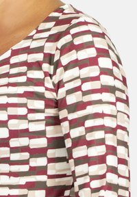 Top multicolor con un patrón geométrico en tonos burdeos, beige y gris. La tela parece suave con una textura blanda.